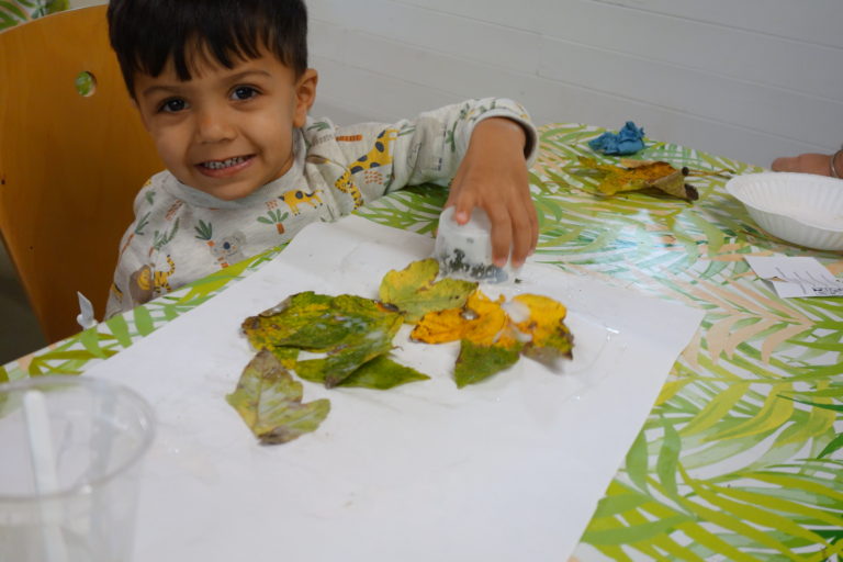 young boy smiling while creating a leaf collage